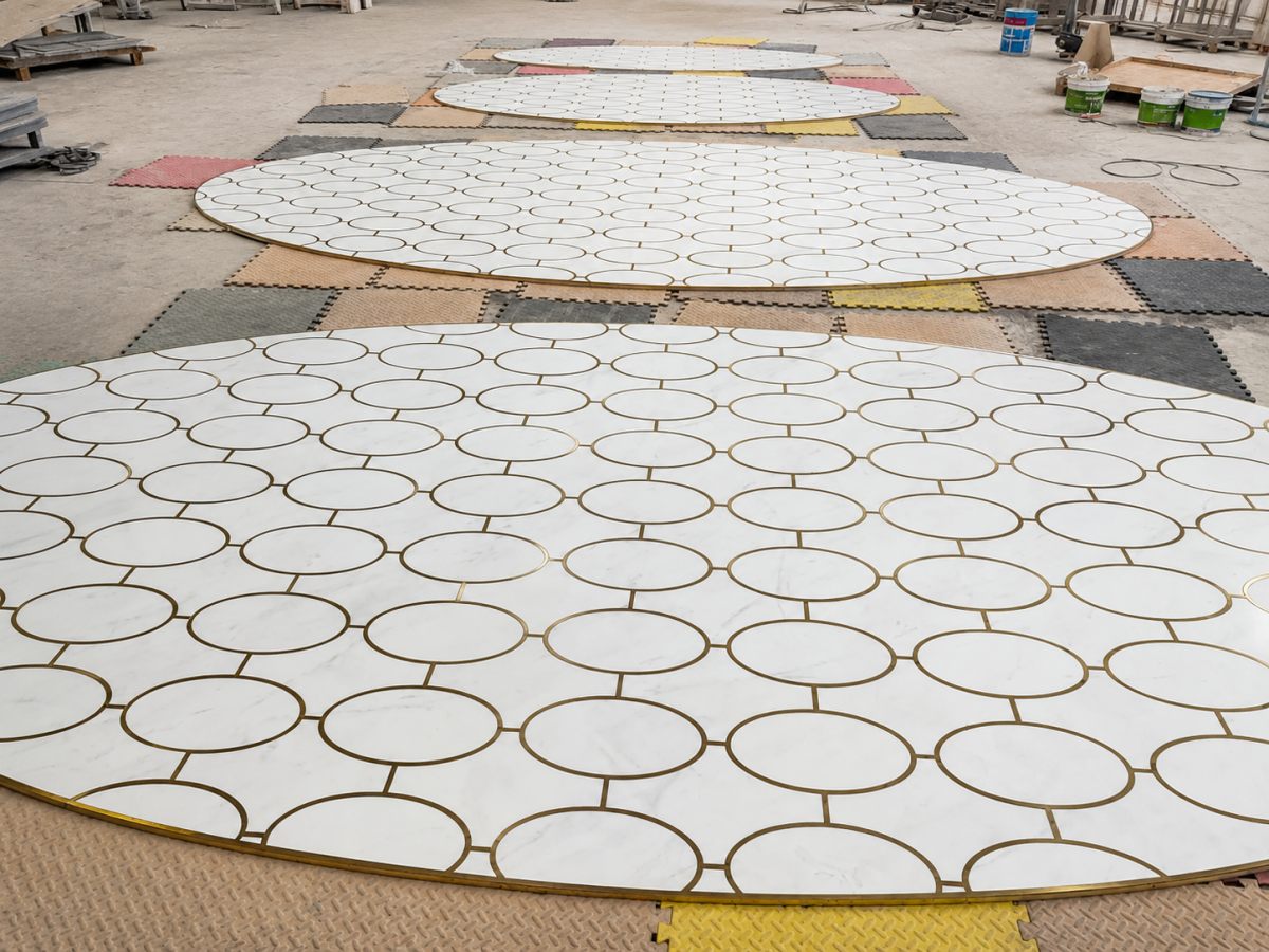 Multiple white marble floor medallion sections with brass inlay laid out for factory inspection